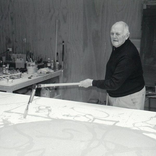 A man in black and white works in an art studio on a large canvas