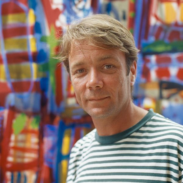 A man in a green and white striped shirt stands in front of a multi-coloured painting