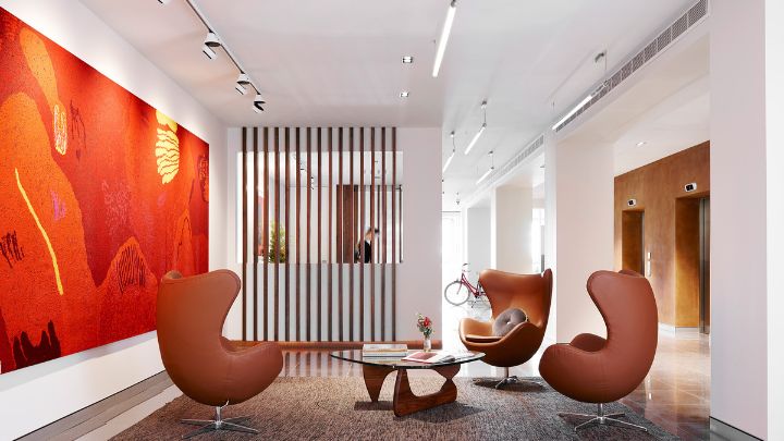 A white and orange-tinged hotel lobby with a large orange wall painting and three chairs